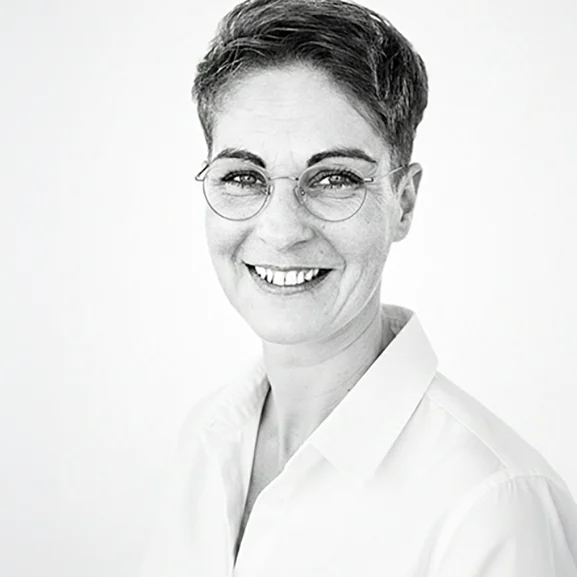 Vanessa Ariane Düvelsdorf - Visual Merchandiserin - VAD Markenspur Vanessa Ariane Düvelsdorf von VAD Markenspur lächelt in die Kamera – Schwarz-Weiß-Porträt mit kurzem Haar und Brille vor hellem Hintergrund